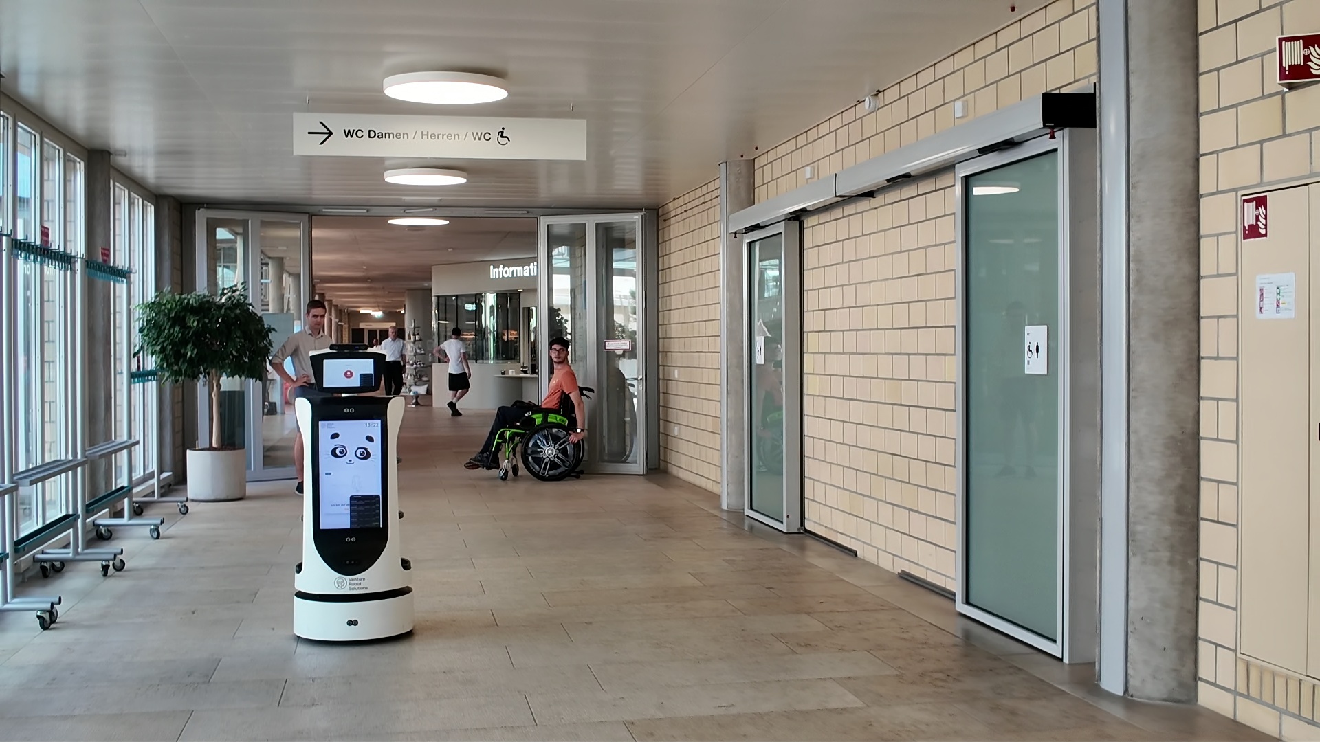 A VRS robot in the corridor of the Swiss Paraplegic Centre, passing a resident in a wheelchair